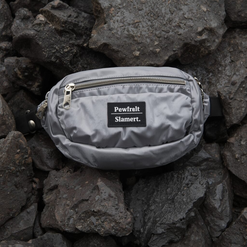 A close-up shot of a nylon fanny pack with a logo, placed on textured rocks, highlighting its 2025 Y2K-inspired utility and sporty appeal.